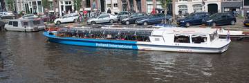 A canal sightseeing boat passing waterside houses and a bridge in Amsterdam.