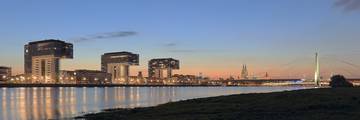 Crane-shaped Rheinauhafen buildings beside the Rhine, with Cologne Cathedral in the distance.