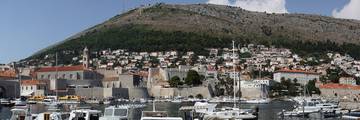 The Old Harbour of Dubrovnik beside the city walls, with houses on the hillside behind.