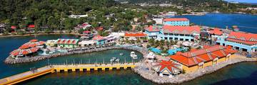 Aerial view of the Port of Roatán in Coxen Hole, with colorful buildings, a pier, and turquoise water.