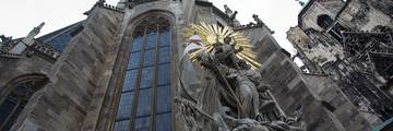 Looking up at St Stephen's Cathedral in Vienna, with a gilded sunburst statue in front of the Gothic windows.